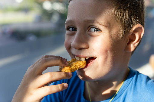 A boy with a pleasant smile enjoys eating delicious nuggets, radiating carefree happiness and simple joys of childhood.