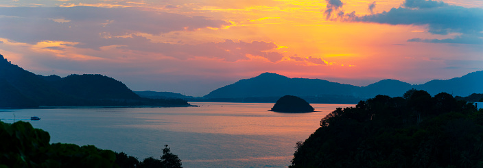 A stunning image of the sun setting over the sea with Koh Samui in the distance. The sky, painted in vibrant shades of orange and pink, reflects off the tranquil waters, creating a picturesque and peaceful end to the day in this beautiful Thai paradise.