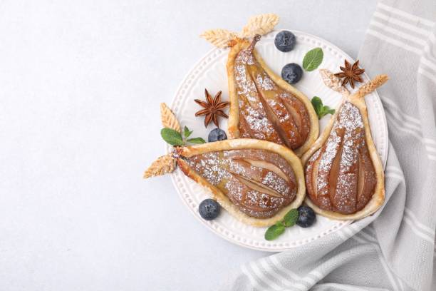 istock Delicious pears baked in puff pastry with powdered sugar on light table, top view. Space for text 1890280507