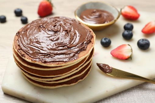 Delicious pancakes with chocolate paste, berries and knife on table, closeup. Space for text