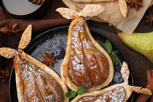Delicious pears baked in puff pastry with powdered sugar served on table, top view