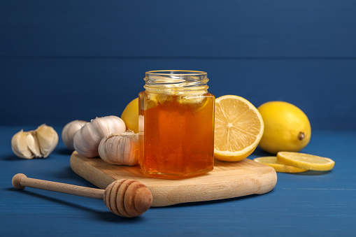 Honey with garlic in glass jar, lemons and dipper on blue wooden table