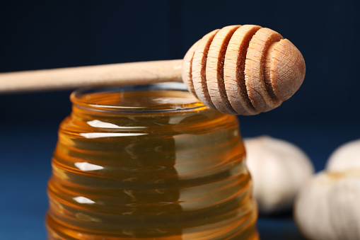 Jar with honey and dipper against blurred background, closeup