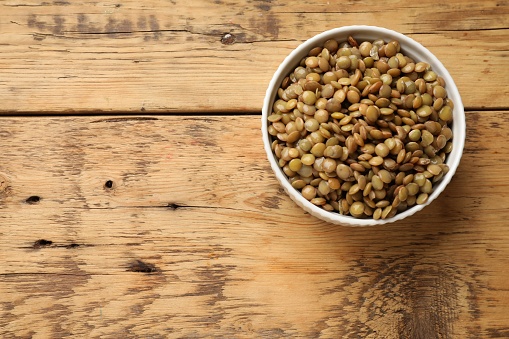 Delicious lentils in bowl on wooden table, top view. Space for text