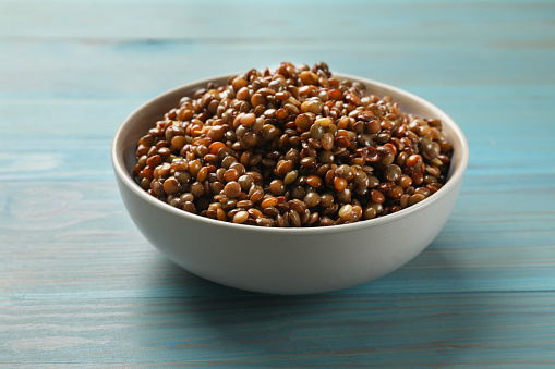 Delicious lentils in bowl on light blue wooden table, closeup