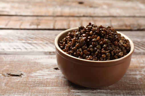 Delicious lentils in bowl on wooden table, closeup. Space for text
