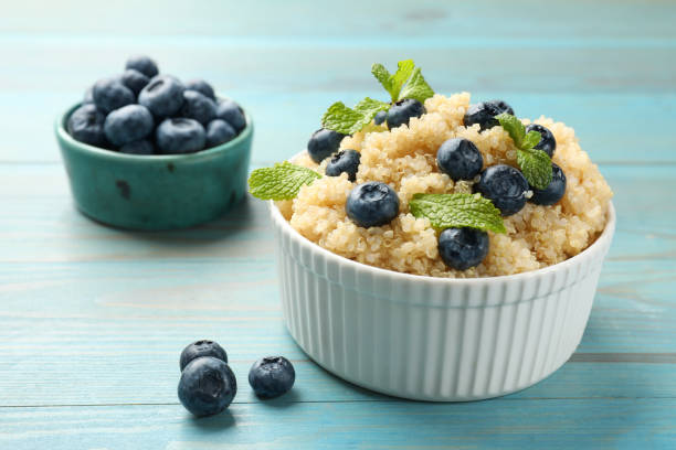 Tasty quinoa porridge with blueberries and mint in bowl on light blue wooden table