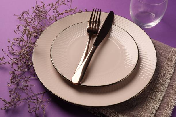 istock Stylish table setting. Plates, cutlery and floral decor on purple background 1890326644