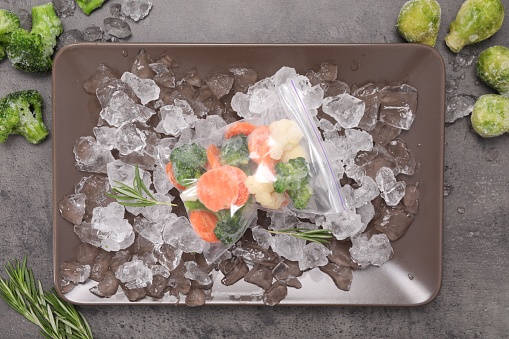 Mix of different frozen vegetables with ice on grey table, flat lay