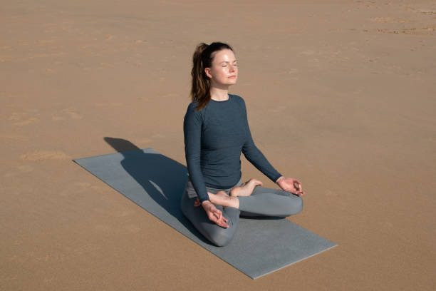 istock Young woman practicing yoga in lotus pose on mat on beach. 1890354495
