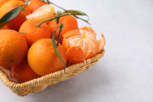 Fresh ripe tangerines with green leaves in wicker basket on white table, closeup. Space for text
