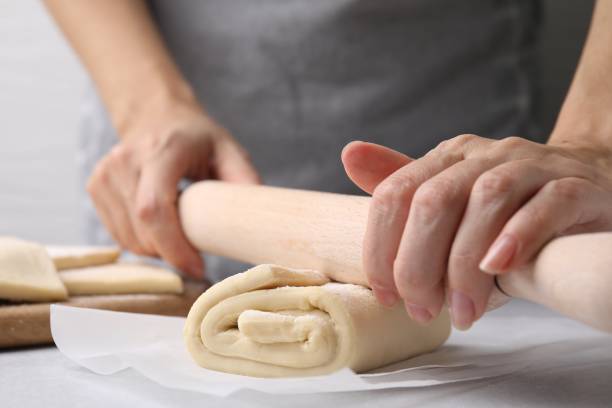 istock Woman rolling raw puff pastry dough at white table, closeup 1890373092
