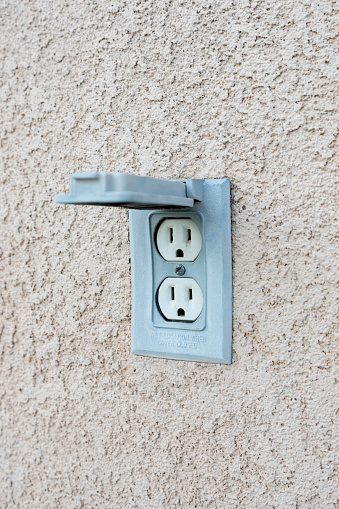 Outdoor electrical outlet with cover in a beige stucco wall.