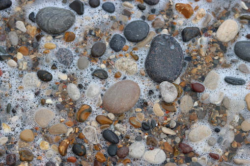 Close up of smooth stones and pebbles on a beach covered in sea foam