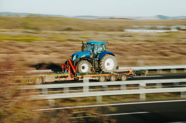 A truck in motion on a highway carrying a brand new tractor