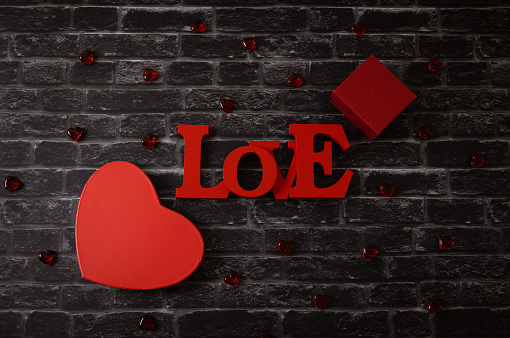 Two gift box in the form of a red heart, a tree word love and a glass heart lies in the center on a black brick background, flat lay closeup. The concept of Valentine's Day, love day.