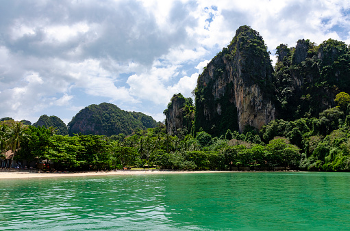 A picturesque image of Railay Beach in Thailand, showcasing its stunning white sandy shores flanked by towering limestone cliffs. This secluded paradise, accessible only by boat, is a haven of tranquility, renowned for its crystal-clear waters and dramatic natural scenery.