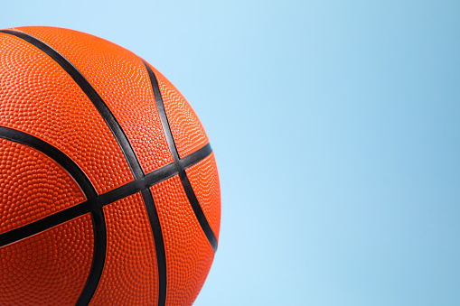 One orange basketball ball on light blue background, closeup. Space for text