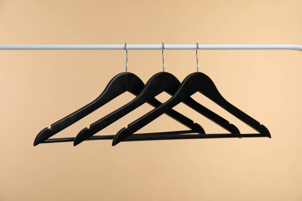 istock Black clothes hangers on rack against beige background 1890473878