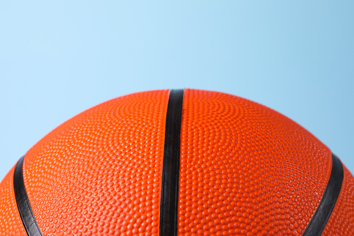 One orange basketball ball on light blue background, closeup