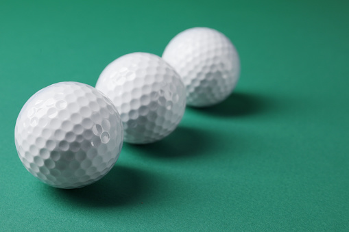 Three golf balls on green background, closeup. Space for text