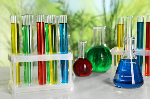 Test tubes with liquids in stand and flasks on table against blurred background