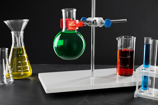 Retort stand and laboratory glassware with liquids on table against black background