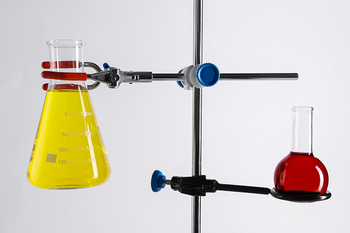 Retort stand and laboratory flasks with liquids on white background