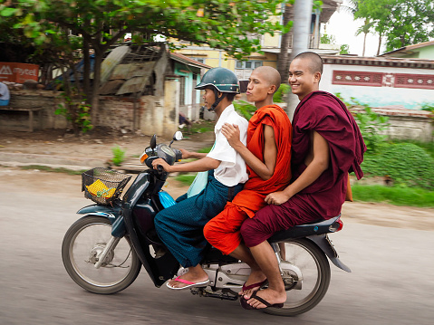 3 people on a scooter. A driver with helmet and and two monks in robes as passengers