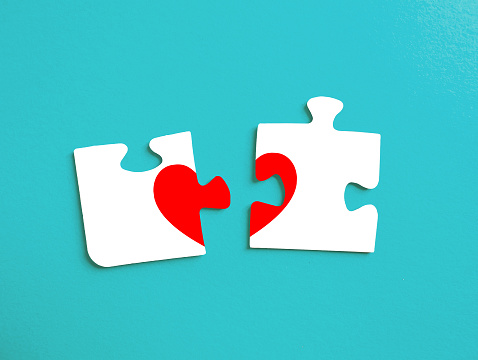 Two separated pieces of a puzzle on a turquoise background with a blank space, depicting the idea of rupture or cooperation