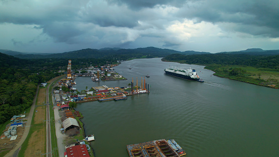 Dark rain clouds rolling over port and cargo ship passing through Panama Canal. Artificial water channel that runs through tropical environment and connects Atlantic and Pacific oceans on a stormy day