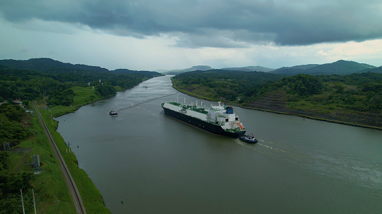 Freighter with an escort travels along a strategic waterway of Panama Canal. Astonishing engineering project that managed to connect Pacific and Atlantic oceans and shorten routes of maritime traffic.