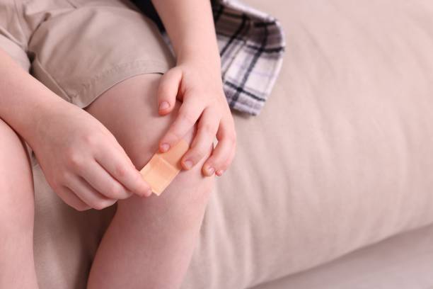 istock Little boy putting sticking plaster onto knee on sofa, closeup. Space for text 1890570485