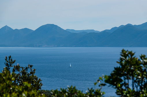 Beautiful view of a distant sailboat sailing peacefully on the blue Adriatic Sea. Incredibly picturesque sea routes between the Croatian Islands and along mountainous coastline of sunny Dalmatia.