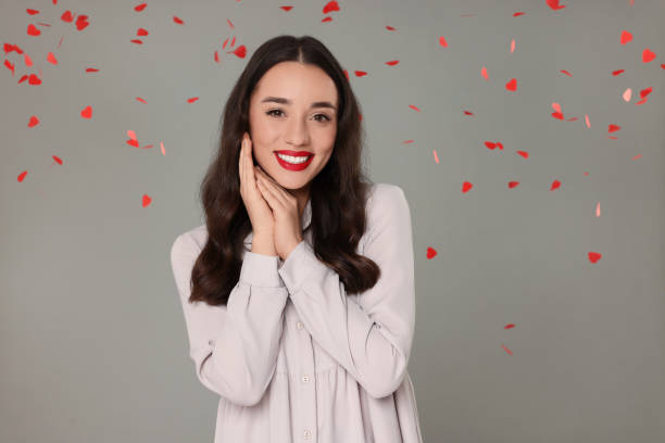 istock Beautiful young woman under falling heart shaped confetti on grey background 1890596776