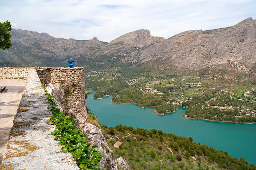 A scenic image of Guadalest, Spain, nestled among the mountains of Alicante. This stunning village, perched atop a granite mountain, is renowned for its historic castle, ancient architecture, and breathtaking views over the valley and reservoir below, encapsulating its rich history and natural beauty.