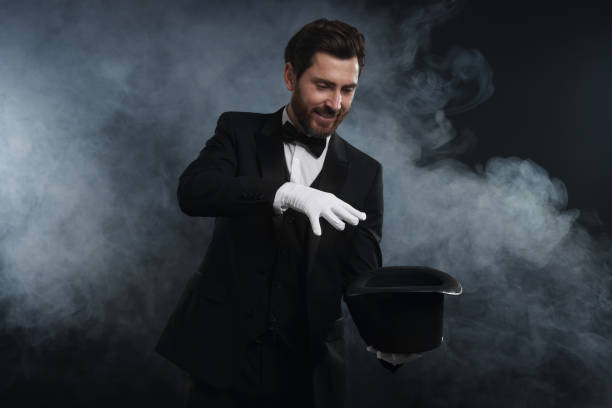 istock Happy magician showing magic trick with top hat in smoke on dark background 1890653400