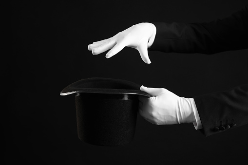 Magician showing magic trick with top hat on black background, closeup