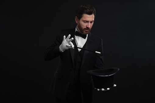 Magician showing magic trick with top hat on black background
