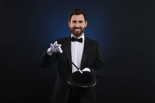 istock Happy magician showing magic trick with top hat on dark blue background 1890656280