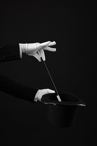 Magician showing magic trick with top hat on black background, closeup