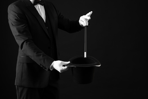 Magician showing magic trick with top hat on black background, closeup. Space for text
