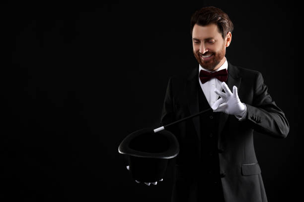 istock Happy magician showing magic trick with top hat on black background, space for text 1890660476