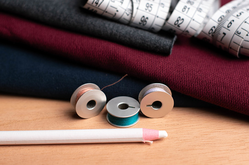 texture of dark red, dark blue and dark gray fabrics, white pencil, spools and plastic meter of threads on a wooden table