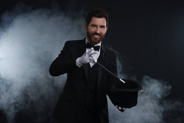 istock Happy magician showing magic trick with top hat in smoke on dark background 1890661007