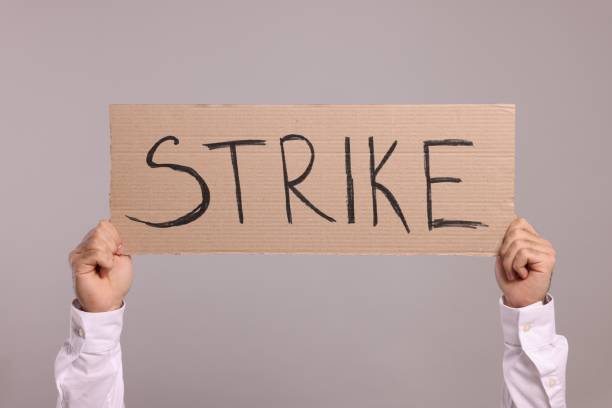 istock Man holding cardboard banner with word Strike on light grey background, closeup 1890685781