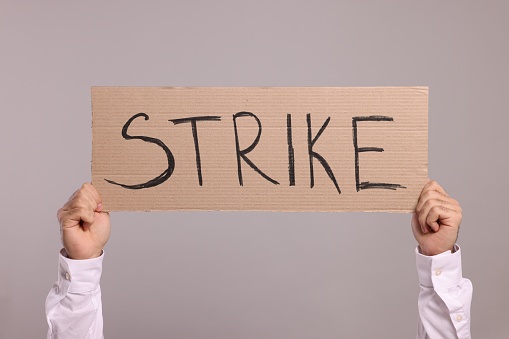 Man holding cardboard banner with word Strike on light grey background, closeup