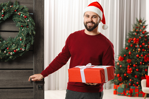 Young man in Santa hat with Christmas gift box received by mail indoors