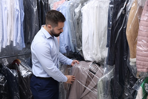 Dry-cleaning service. Worker taking jacket from rack indoors