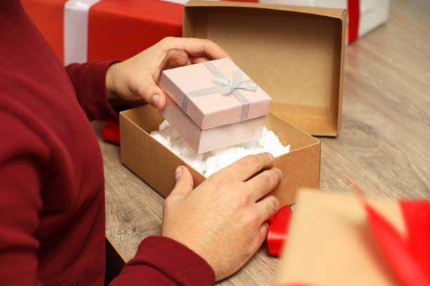 istock Man putting Christmas gift box into parcel at wooden table, closeup. Sending present by mail 1890691509